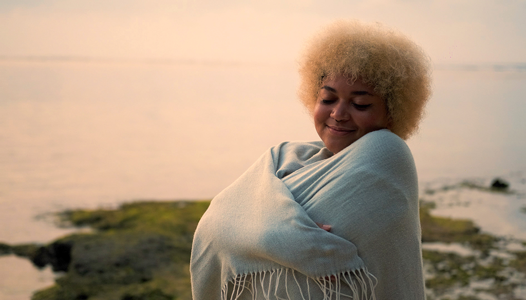 Woman wrapping herself in a blanket on the beach smiling with comfort